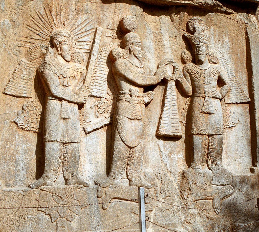 The Yazata Mithra — At Taq-e Bostan, radiate Mithra stands on the lotus behind the king, the barsom in his hands.